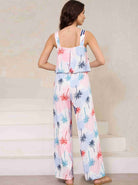 Frau in sommerlichem Jumpsuit mit Palmenmuster, ärmellos, pastellfarben, ideal für Strandmode und Freizeitkleidung. Perfekt für warme Tage.