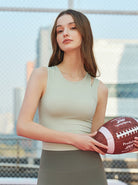 Frau in Sportbekleidung hält American Football, steht vor einem Maschendrahtzaun. Keywords: Sportmode, American Football, Fitness, Outdoor.