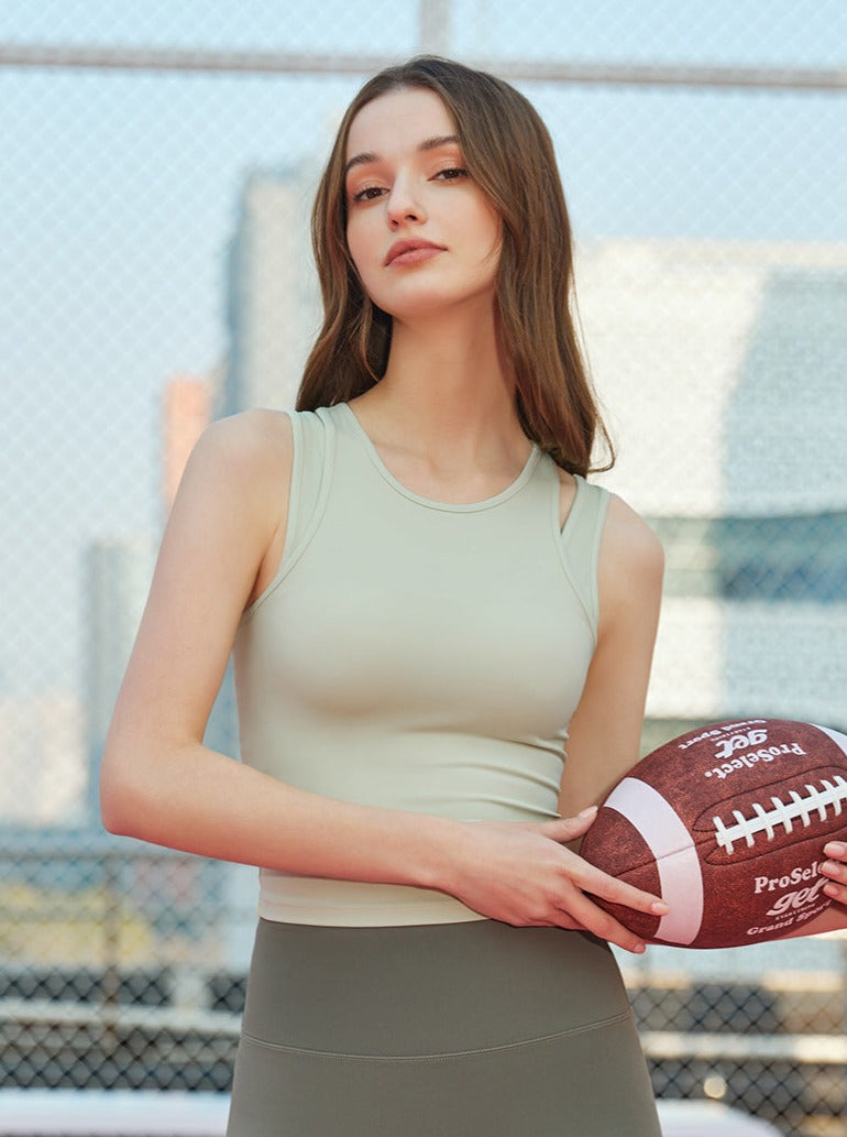 Frau in Sportbekleidung hält American Football, steht vor einem Maschendrahtzaun. Keywords: Sportmode, American Football, Fitness, Outdoor.
