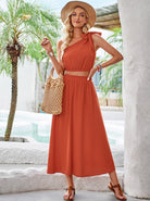 Frau in elegantem, orangefarbenem Sommerkleid mit Strohhut und geflochtener Tasche, posiert vor tropischem Hintergrund. Sommermode, Damenbekleidung.