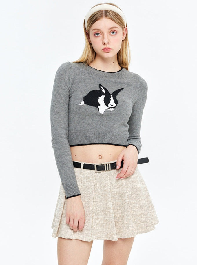 Grauer Pullover mit Hasenmotiv, kombiniert mit beigem Faltenrock. Modetrend, Damenbekleidung, stilvoller Look, Herbstmode.