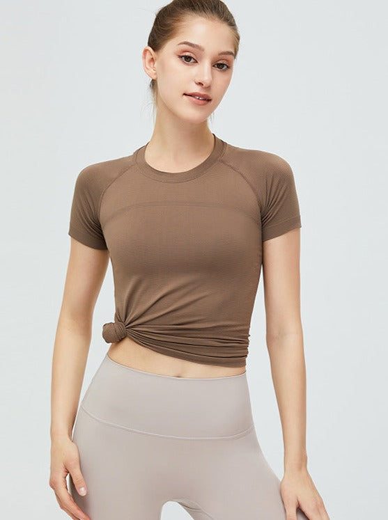 Frau in braunem Sport-T-Shirt und grauer Leggings, Fitnessmode, athletische Kleidung, bequeme Sportbekleidung, trendiger Freizeitlook.
