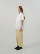 Frau in weißem Oversize-T-Shirt und beigen Hosen, seitlich stehend. Minimalistischer Stil, lässige Mode, moderne Damenbekleidung.