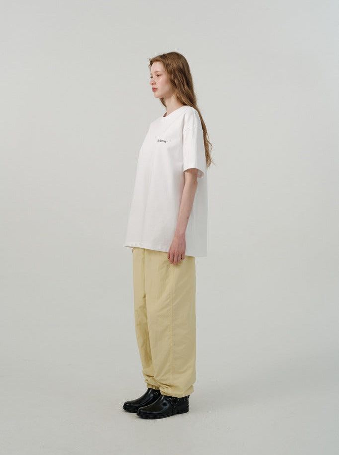 Frau in weißem Oversize-T-Shirt und beigen Hosen, seitlich stehend. Minimalistischer Stil, lässige Mode, moderne Damenbekleidung.