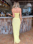 Frau in gelbem Sommerkleid an einer Bar, Rückenansicht. Perfekt für Strandmode, Sommeroutfits, stilvolle Freizeitkleidung.