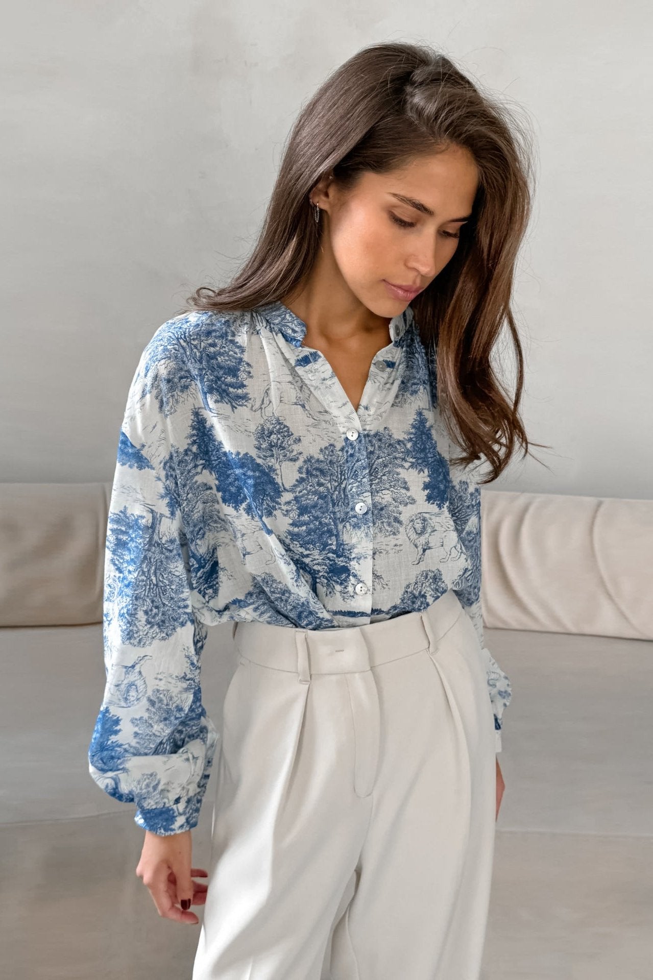 Elegante Frau in weißer Bluse mit blauem Toile-de-Jouy-Muster, kombiniert mit stilvollen, weißen Hosen. Perfekt für modische Büro-Outfits.