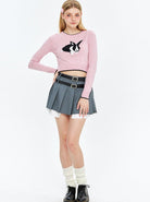 Junge Frau in rosa Pullover mit Hasenmotiv, grauem Faltenrock und schwarzen Stiefeln. Modetrend, Streetwear, jugendlicher Stil, lässig.