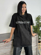 Frau in schwarzem Oversize-T-Shirt mit russischem Schriftzug, lächelt, steht vor einer Kommode. Modetrend, Streetwear, lässiger Stil.