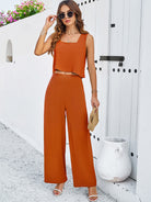Frau in stilvollem, orangefarbenem Zweiteiler, bestehend aus ärmellosem Top und weiten Hosen, posiert vor weißer Wand. Sommermode, Damenbekleidung.