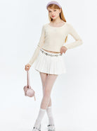 Frau in modischem Outfit: cremefarbener Pullover, weißer Faltenrock, rosa Tasche. Trendige Damenmode, eleganter Look, stilvolle Accessoires.