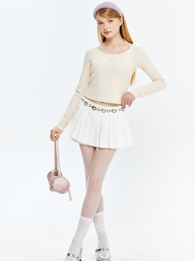 Frau in modischem Outfit: cremefarbener Pullover, weißer Faltenrock, rosa Tasche. Trendige Damenmode, eleganter Look, stilvolle Accessoires.