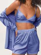 Frau in blauer Satin-Pyjama-Set: Top, Shorts und Hemd. Elegante Nachtwäsche, bequem und stilvoll. Perfekt für Damenmode und Loungewear.
