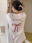 Frau in weißem T-Shirt mit Aufdruck "La Vie en Rose" und roter Schleife. Modetrend, lässiger Stil, Sommermode, Damenbekleidung.