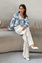 Elegante Frau in weißer Hose und blauer Bluse sitzt auf einem Sofa. Modetrends, Damenmode, stilvolle Kleidung, zeitloser Chic.