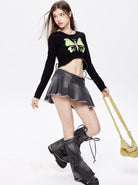 Junge Frau in modischem Outfit: schwarzes Crop-Top mit Schmetterlingsmotiv, grauer Minirock, hohe Stiefel. Trendige Damenmode, Streetwear.