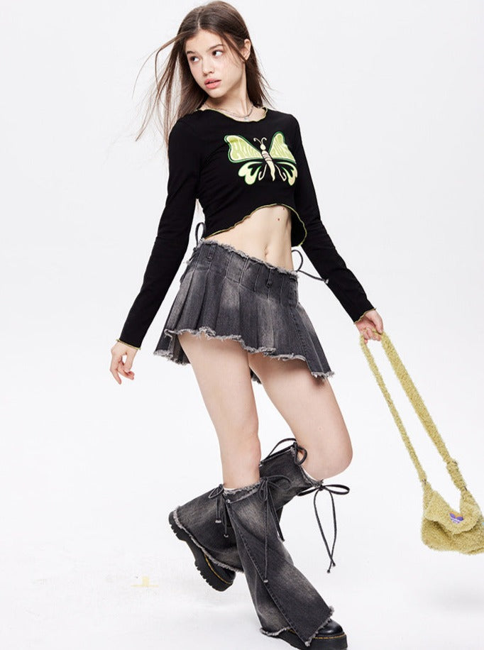 Junge Frau in modischem Outfit: schwarzes Crop-Top mit Schmetterlingsmotiv, grauer Minirock, hohe Stiefel. Trendige Damenmode, Streetwear.