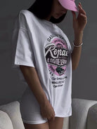 Frau in weißem Oversize-T-Shirt mit Auto-Reparatur-Print, kombiniert mit rosa Baseballkappe. Modetrend, lässiger Streetstyle, urbaner Look.