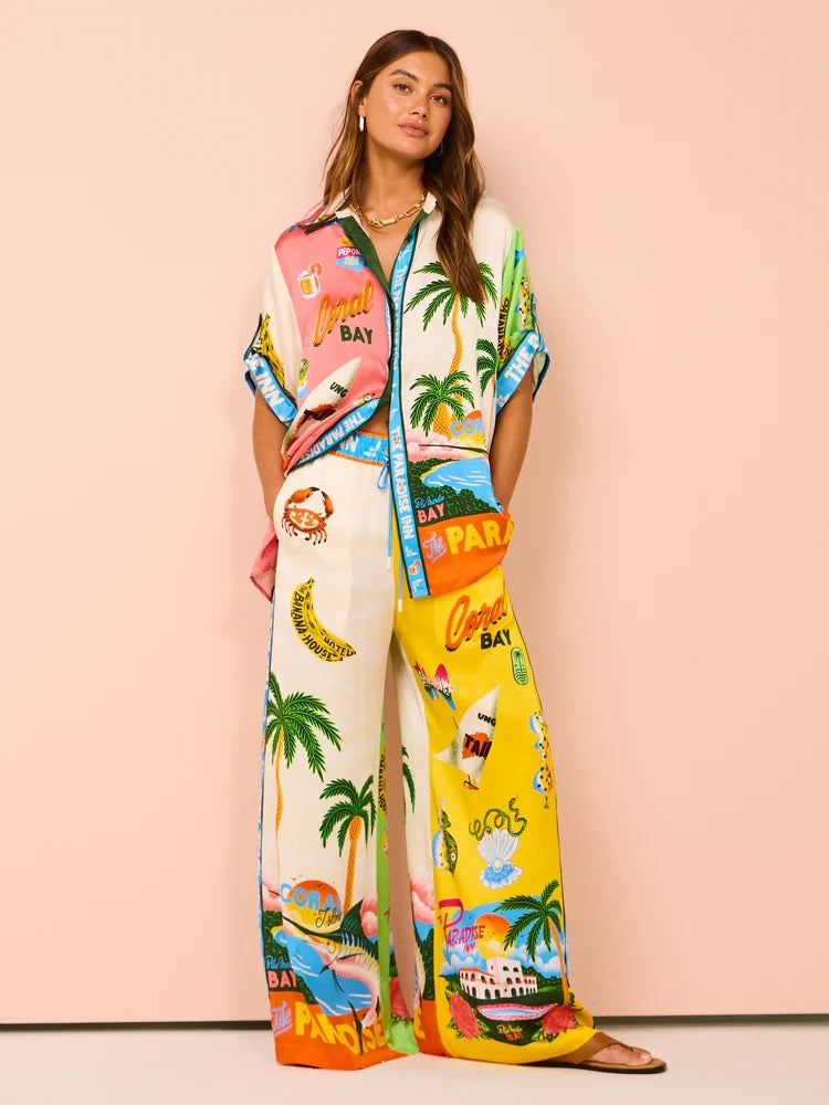 Frau in bunter, tropisch bedruckter Pyjama-Set mit Palmen und Strandmotiven. Modetrend, Sommermode, bequeme Nachtwäsche, Damenbekleidung.