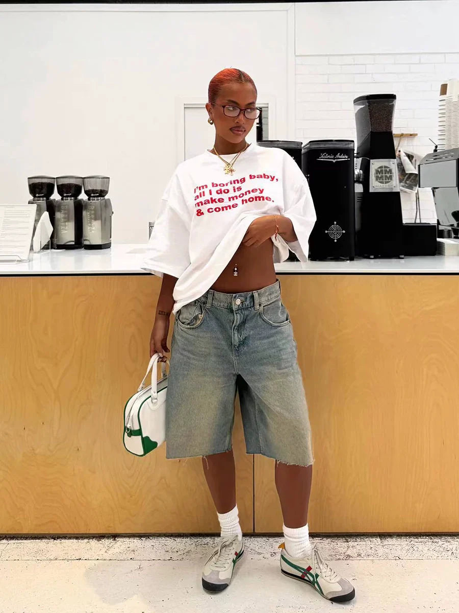 Frau in lässigem Outfit mit weißem T-Shirt und Jeansshorts, steht vor einer modernen Kaffeebar. Trendige Mode, urbaner Stil, Streetwear.
