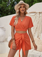 Frau in orangefarbenem Sommeroutfit mit Strohhut, vor mediterraner Kulisse. Modetrend, Sommermode, Damenbekleidung, stilvoll, elegant.