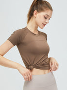 Frau in braunem Sport-T-Shirt, geknotet, mit beiger Leggings. Fitnessmode, athletische Kleidung, bequeme Sportbekleidung für Damen.