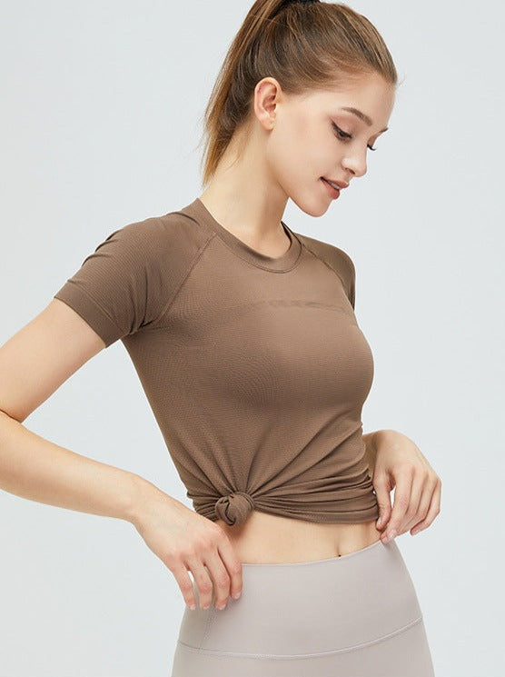 Frau in braunem Sport-T-Shirt, geknotet, mit beiger Leggings. Fitnessmode, athletische Kleidung, bequeme Sportbekleidung für Damen.