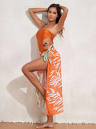 Frau in orangefarbenem Badeanzug mit tropischem Muster, posiert vor hellem Hintergrund. Sommermode, Strandkleidung, stilvoller Look.