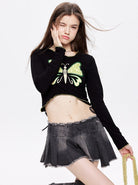 Junge Frau in schwarzem Langarmshirt mit Schmetterlingsmotiv und grauem Faltenrock. Modetrend, Streetwear, jugendlicher Stil, lässig.