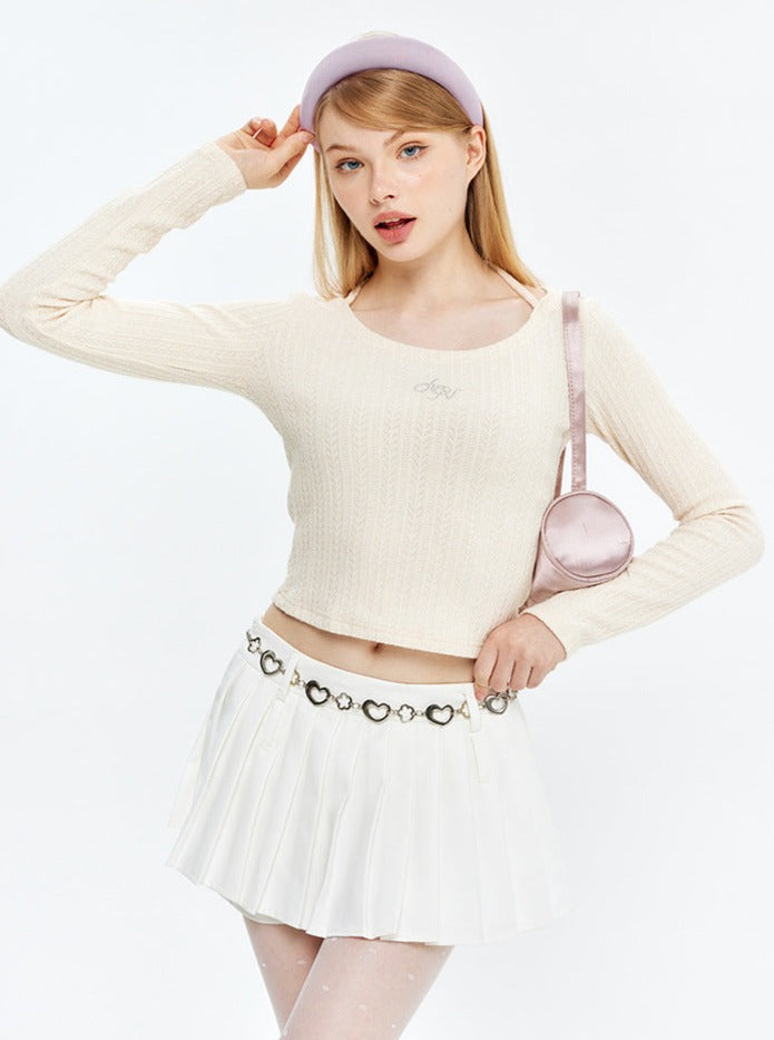 Junge Frau in modischem, cremefarbenem Strickpullover und weißem Faltenrock, trägt eine rosa Umhängetasche. Trendige Damenmode, elegant und stilvoll.