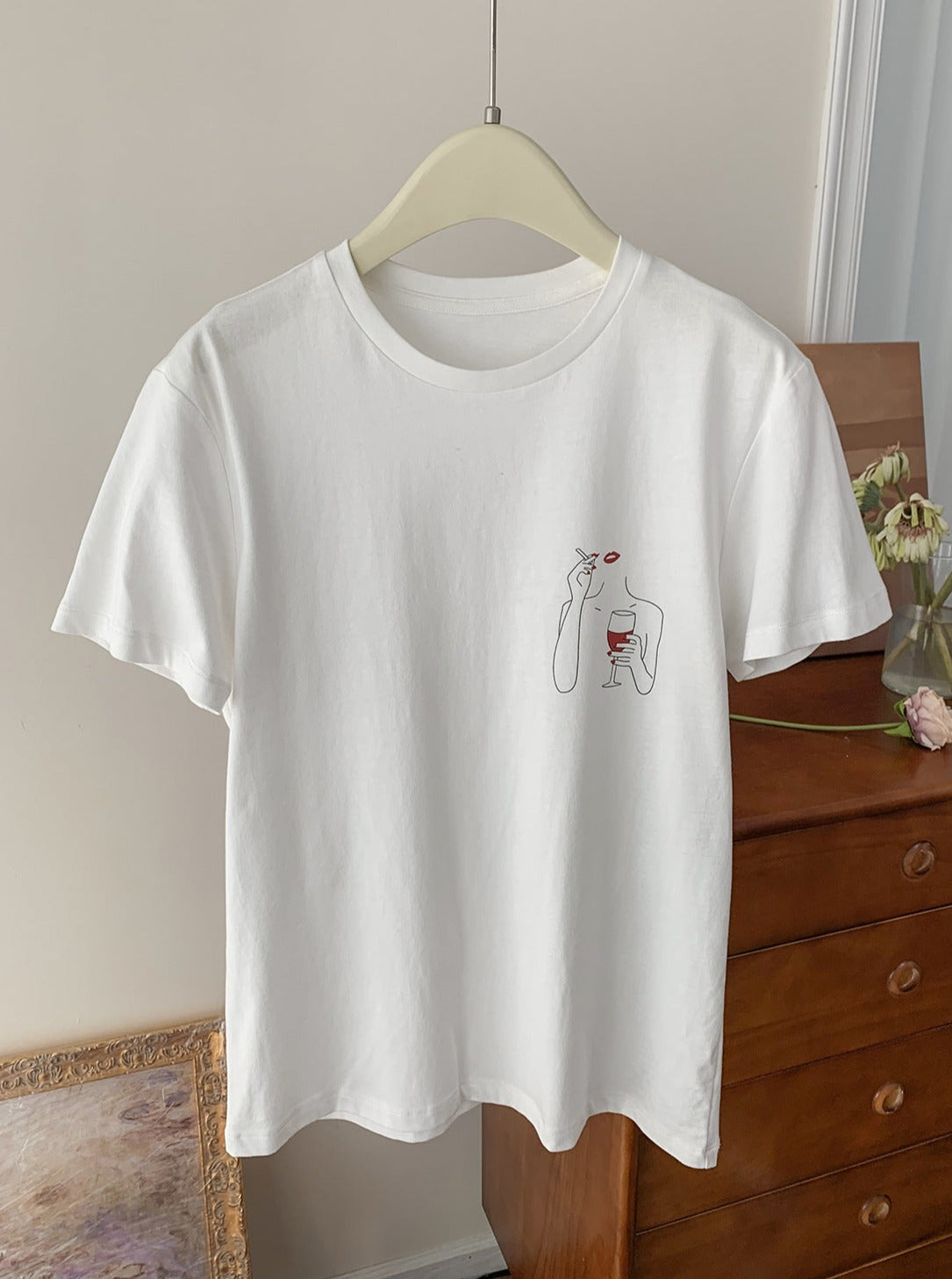 Weißes T-Shirt mit minimalistischem Design, Weinmotiv, aus Baumwolle, hängend auf Holzkleiderbügel. Perfekt für lässige Mode-Looks.