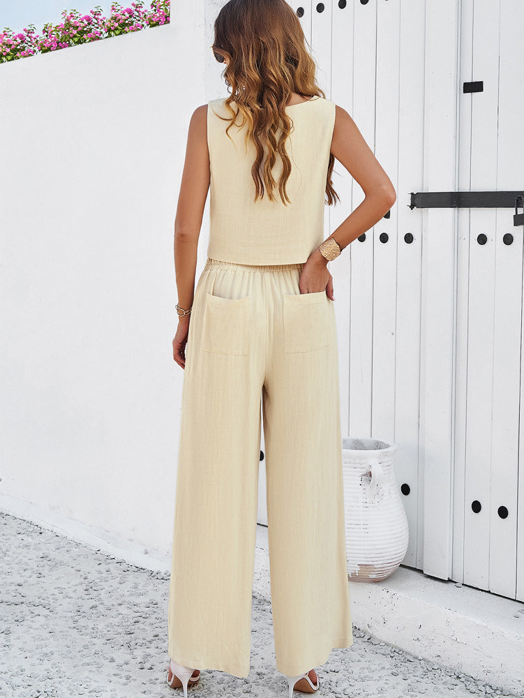 Frau in eleganter, beiger Leinenhose und ärmellosem Top vor weißer Wand. Sommermode, Damenbekleidung, stilvoll, lässig, modern.
