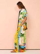 Frau in farbenfrohem, tropischem Maxikleid mit Palmen- und Strandmotiven, ideal für Sommermode und Strandurlaub. Trendiges, luftiges Design.