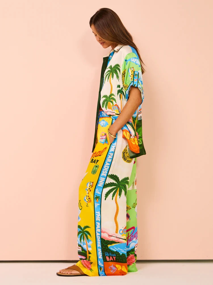 Frau in farbenfrohem, tropischem Maxikleid mit Palmen- und Strandmotiven, ideal für Sommermode und Strandurlaub. Trendiges, luftiges Design.