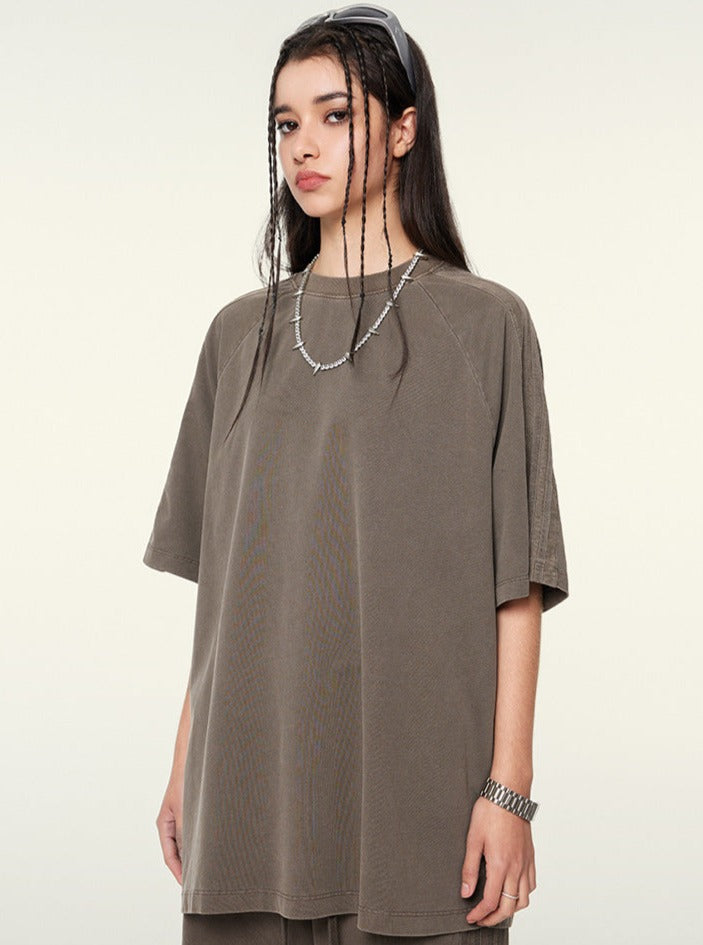 Frau in oversized braunem T-Shirt, lässiger Streetwear-Look, lange Haare, modische Kette, urbaner Stil, trendige Damenmode, minimalistisch.