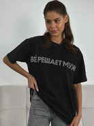 Frau trägt schwarzes T-Shirt mit russischem Schriftzug, kombiniert mit grauen Jeans. Modetrend, lässiger Stil, urbaner Look, Streetwear.