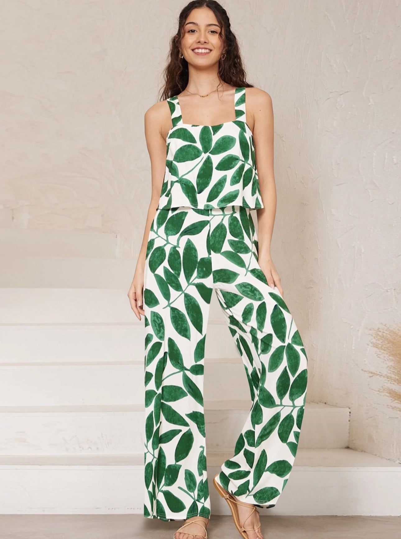 Frau in modischem, ärmellosem Jumpsuit mit grünem Blattmuster, ideal für Sommermode. Perfekt für trendige, lässige Outfits und stilvolle Looks.