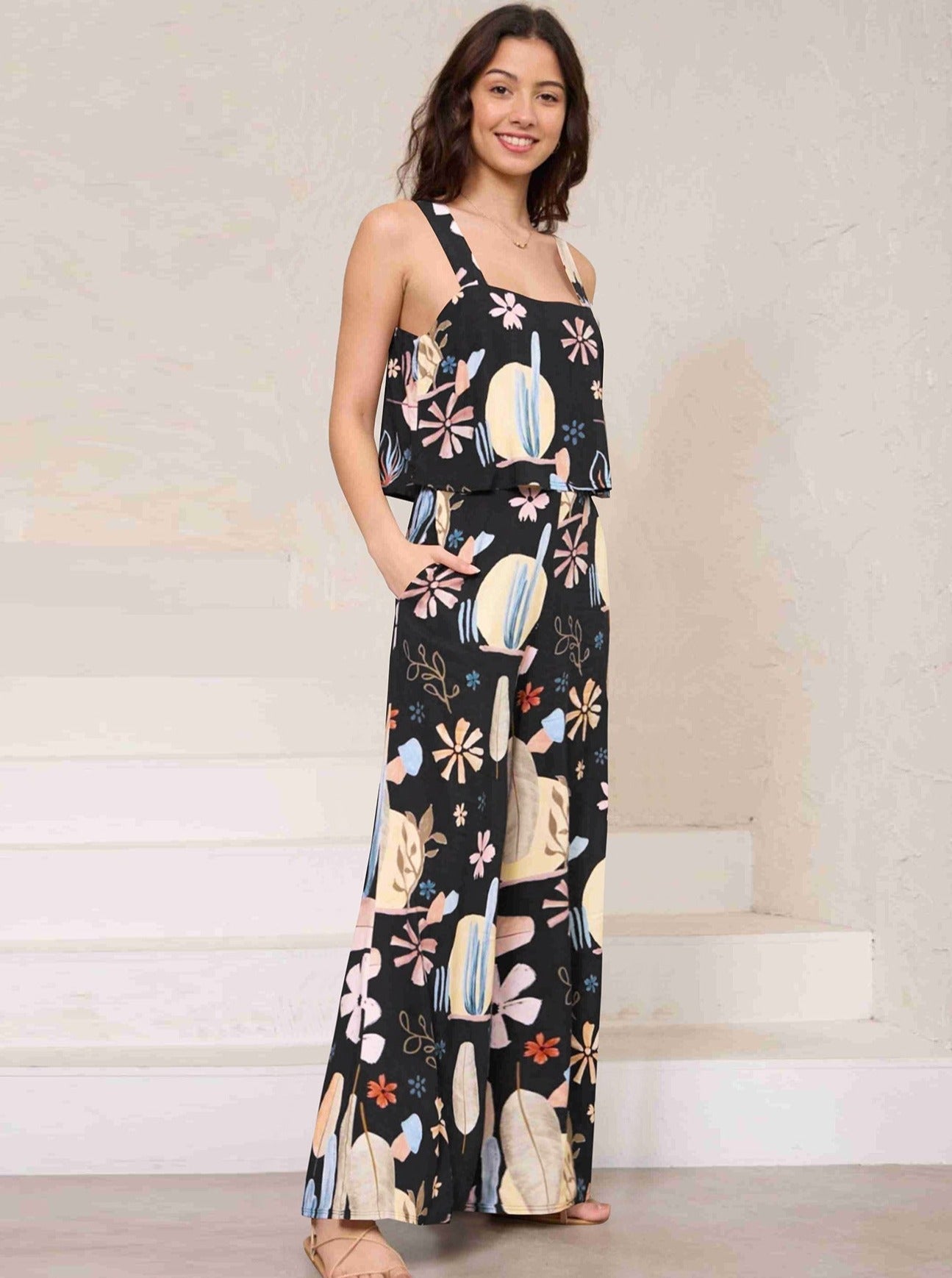 Frau in schwarzem, geblümtem Jumpsuit, lässig und modisch, ideal für Sommermode. Perfekt für Freizeit und Strand. Eleganter, bequemer Look.