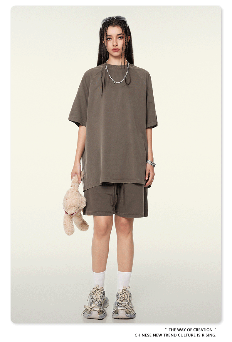 Frau in oversized braunem T-Shirt und Shorts, hält ein Plüschtier, trägt modische Sneaker. Trendige Streetwear, lässiger Look, urbaner Stil.