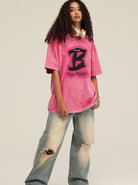 Junge Frau in übergroßem, pinkem T-Shirt mit schwarzem Logo, kombiniert mit weiten, zerrissenen Jeans und Kopfhörern. Trendige Streetwear-Mode.