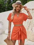 Frau in orangefarbenem Sommeroutfit mit Strohhut und Tasche, vor weißem Hintergrund. Perfekt für Strandmode, Sommerkleidung, Damenmode.