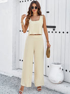 Frau in eleganter, beiger Sommerkleidung vor weißer Tür, trägt Sonnenbrille und Sandalen. Perfekt für stilvolle Sommermode und Freizeitoutfits.