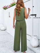 Frau in grünem Jumpsuit vor weißer Wand, Sommermode, lässiger Stil, ärmelloses Top, weite Hose, modische Damenbekleidung, Outdoor-Fotoshooting.