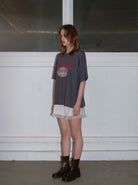 Frau in grauem Oversize-T-Shirt und weißem Spitzenrock, kombiniert mit braunen Stiefeln. Modetrend, lässiger Stil, urbaner Look.