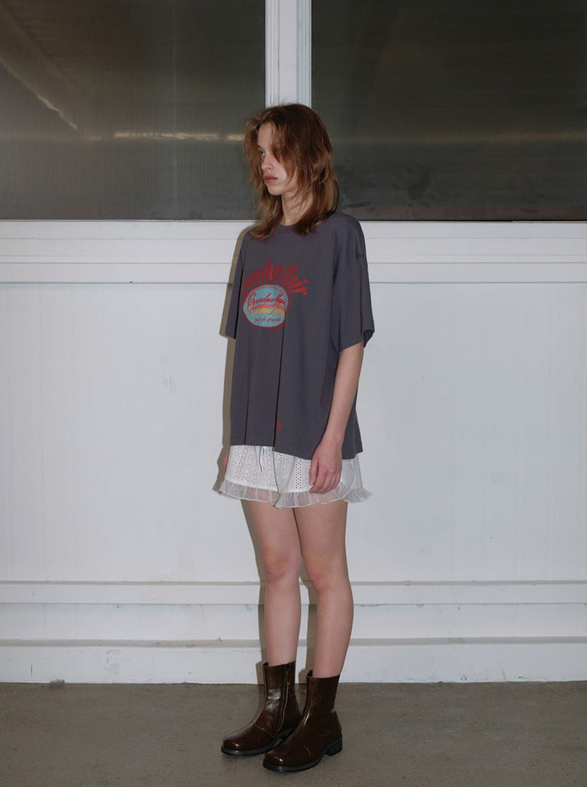 Frau in grauem Oversize-T-Shirt und weißem Spitzenrock, kombiniert mit braunen Stiefeln. Modetrend, lässiger Stil, urbaner Look.