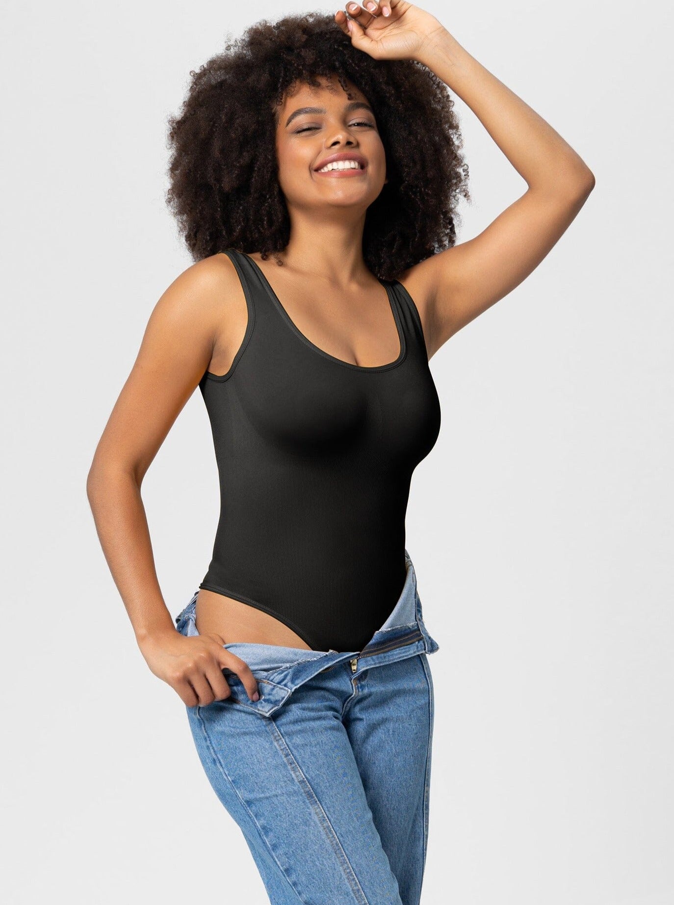 Frau in schwarzem Body und blauer Jeans, lächelnd. Modetrend, Damenbekleidung, Freizeitlook, stilvoll, bequem, Alltagsmode.