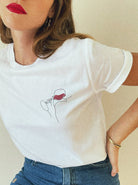 Frau trägt weißes T-Shirt mit minimalistischer Weinglas-Grafik, kombiniert mit blauer Jeans. Modetrend, lässiger Stil, Damenbekleidung.