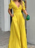 Frau in gelbem Maxikleid mit Puffärmeln und tiefem V-Ausschnitt, hält grüne Clutch. Elegante Abendmode, stilvoll und modern.
