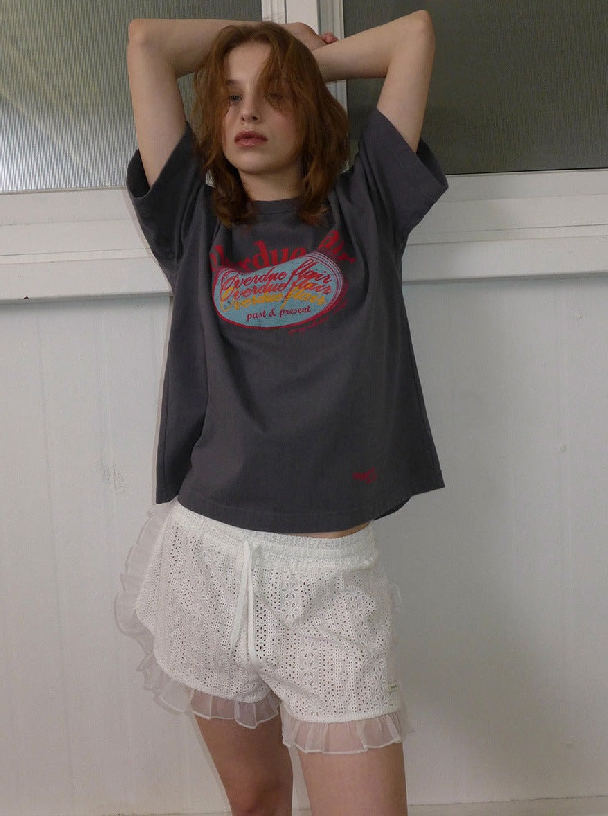 Frau in grauem T-Shirt mit rotem Aufdruck und weißen Spitzen-Shorts. Modetrend, lässiger Look, Sommeroutfit, Damenmode, Streetstyle.