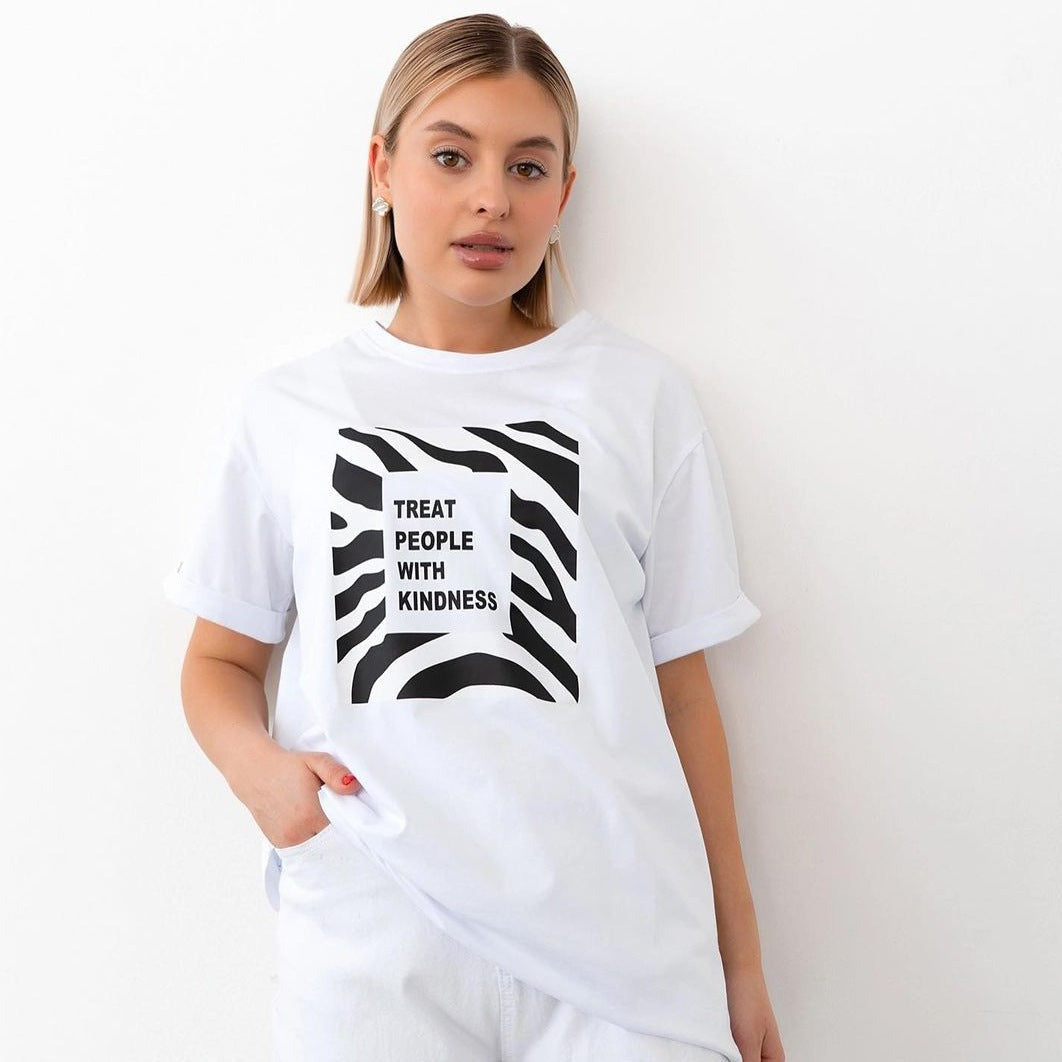 Frau trägt weißes T-Shirt mit "Treat People With Kindness"-Aufdruck und Zebramuster. Modetrend, Statement-Shirt, lässiger Stil, Damenmode.