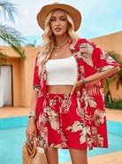 Frau in rotem tropischen Outfit mit Blattmuster, Strohhut und Strohtasche am Pool. Sommermode, Strandkleidung, tropischer Stil.